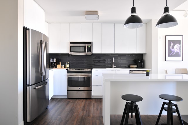 A white kitchen with black fridge and bar chairs