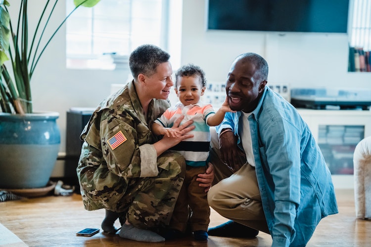 A woman in a military uniform hugging her husband and child.