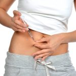 Woman make medical diabetes insulin injection shot into abdomen with single use syringe and text copy space on a white background