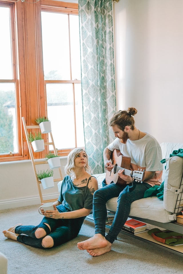 a man playing a guitar to a women holding a coffee cup